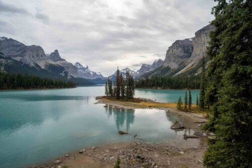 Serene lake in Banff National Park with a small island of trees, surrounded by towering mountains under a cloudy sky. (Photographer: Davey Gravy)