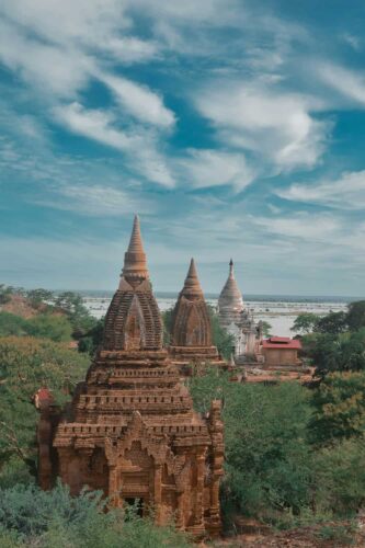 Ancient pagodas in Bagan, Myanmar, with intricate brick structures surrounded by greenery under a vast blue sky, showcasing a serene historic landscape. (Photographer: Lwin Moe Aung)