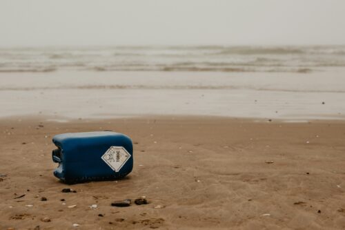 Empty plastic carton sits on the sand next to a dirty ocean shore.