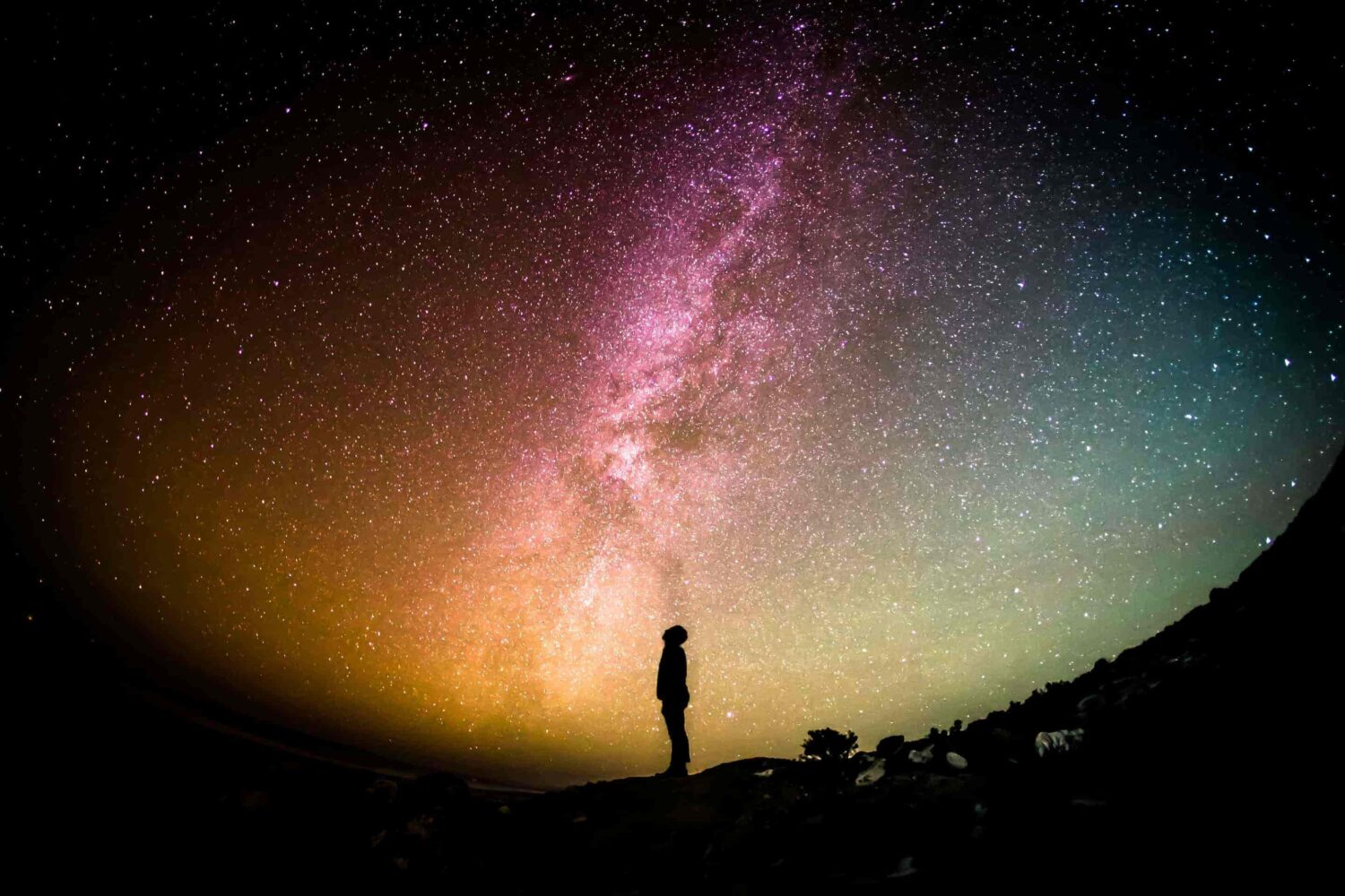 A silhouette of a man looking at a colorful and bright star-filled sky.