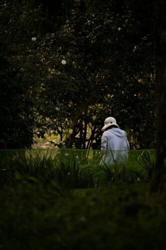 An elderly woman wearing a hat, standing in a garden.