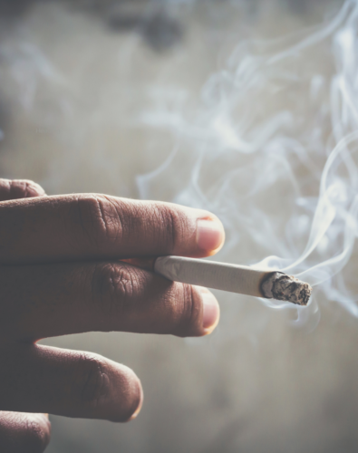 Person holding cigarette and smoking. Smoke coming out.