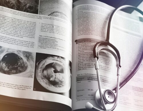 Open medical textbook with images of heart valve complications, accompanied by a stethoscope resting on the pages.