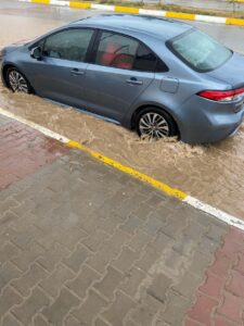 a blue car on a flooded street near a sidewalk