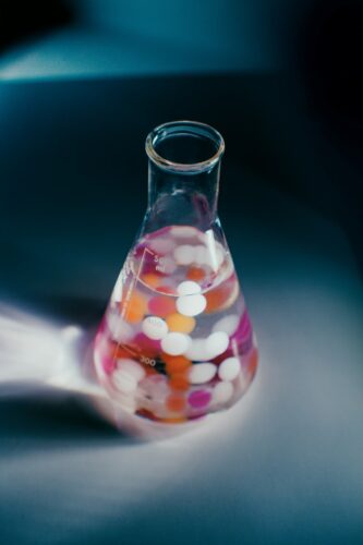 Erlenmeyer flask filled with pink, orange and white particles on lab desk.