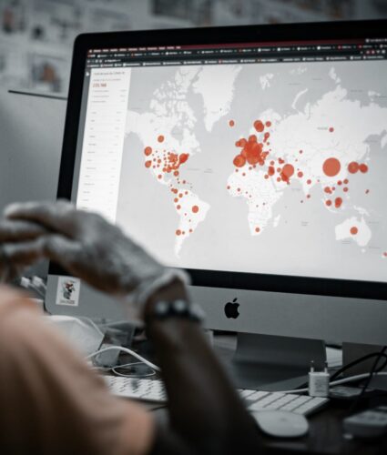 Person viewing a computer screen displaying a world map with red circles indicating data points.