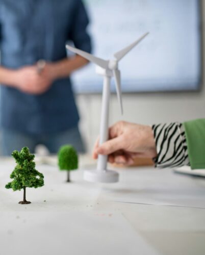A group studies a model of green trees and a wind turbine on a table, with an emphasis on sustainable development and clean energy.