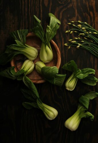 Full heads of baby bok choy are arranged on a wooden table.